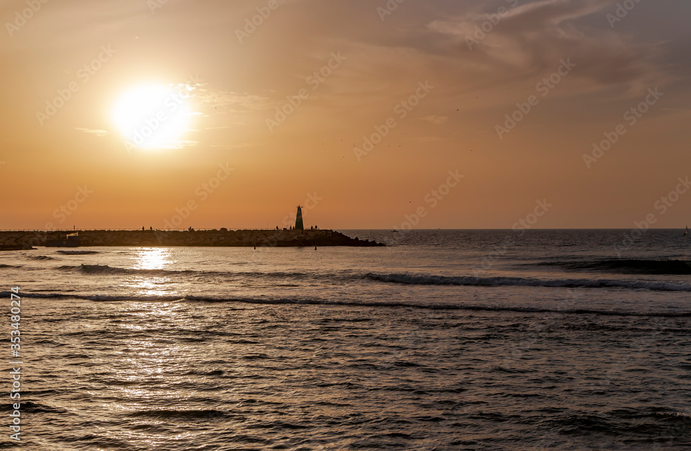 Stone breakwater with a small lighthouse in the Mediterranean at sunset