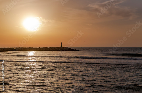 Stone breakwater with a small lighthouse in the Mediterranean at sunset © Tanya Keisha