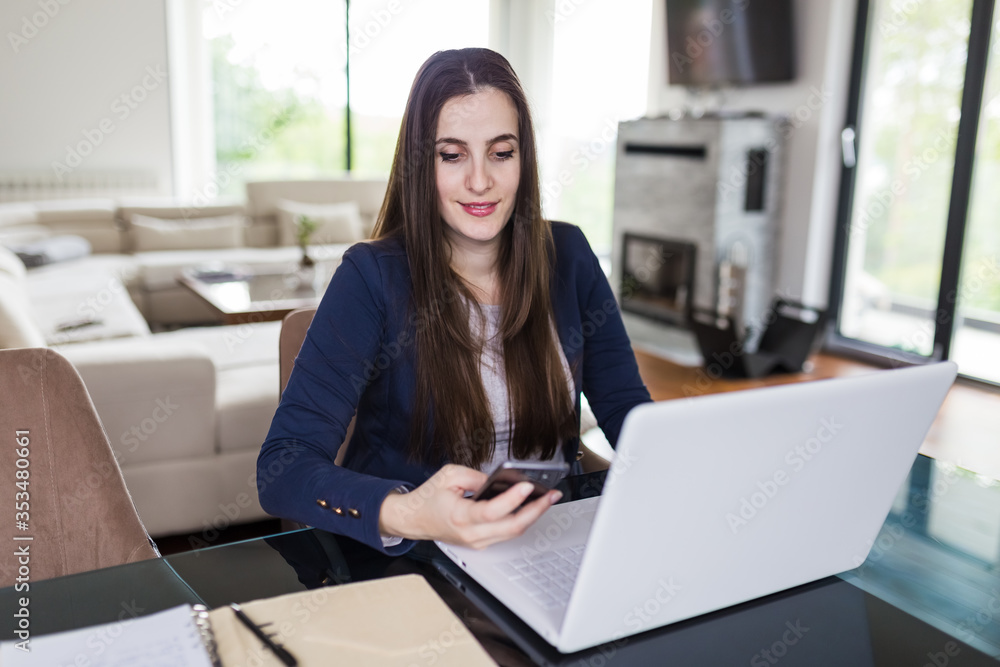 Young woman working from home, holding mobile phone and using laptop at the desk. Online meeting concept. Young woman working from home, holding mobile phone and using laptop at the desk. Online meeting concept.