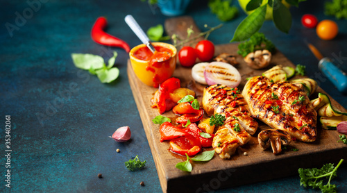 Grilled chicken breasts and different vegetables ad mushroom cooked on a BBQ served on wooden board. Close up view. Concept homemade summer barbeque dinner photo