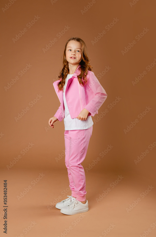 Obraz premium little girl in a pink tracksuit on a beige background