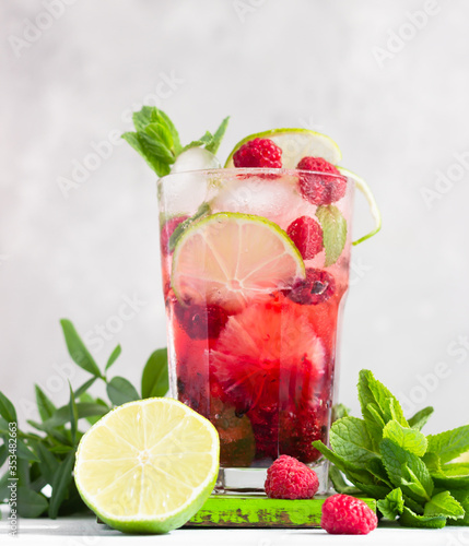 Pink cocktail or lemonade with raspberries, mint, lime and ice on a grey concrete table. Summer refreshment drink.