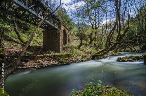 Vouraikos river is flowing under the bridge where the "Odontotos" rack railway train passes. Beautiful nature surrounds the river and bridge creating an idyllic scenery. Peloponnese, Greece. Sunny day