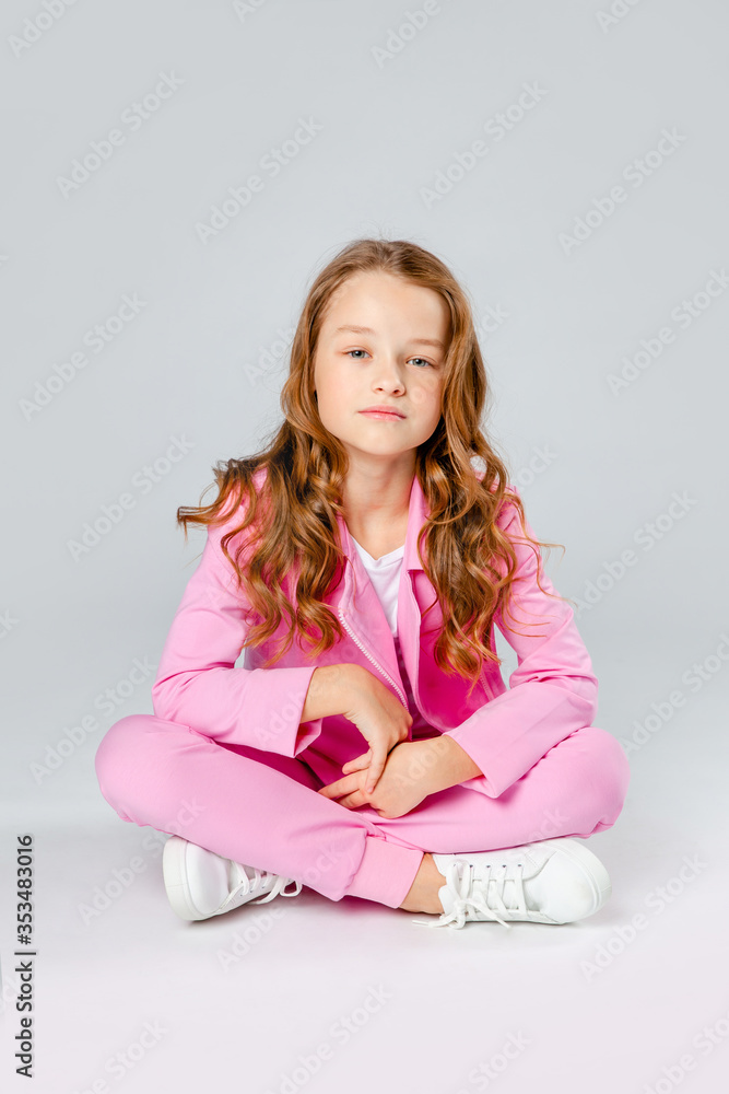 girl in a pink tracksuit and sneakers sits on a light gray background girl in a pink tracksuit and sneakers sits on a light gray background