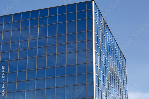 Part of a glass mirrored office building reflecting the blue sky.