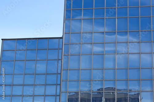 Part of a glass mirrored office building reflecting the blue sky.