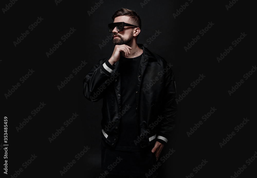 Young man with beard in black
jacket and glasses. Portrait of guy on dark background. Young man with beard in black
jacket and glasses. Portrait of guy on dark background.