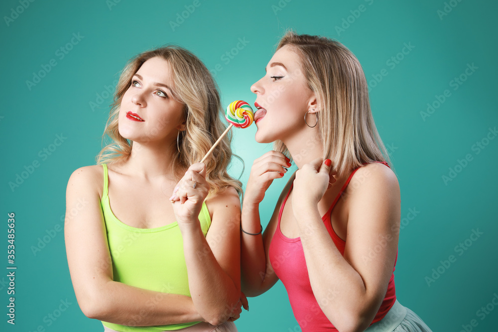 Two twins women holding colorful lollipops and having fun in studio isolated on green background . Two twins women holding colorful lollipops and having fun in studio isolated on green background .