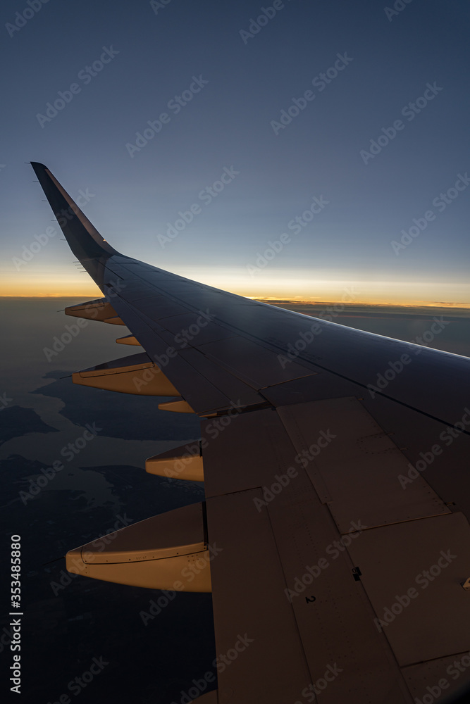 Fototapeta premium Aircraft wing silhouette seen through window in sunset sky with colorful clouds