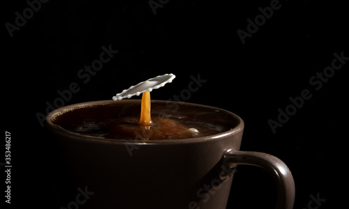 Milk droplet hitting the surface of hot coffee isolate over black background