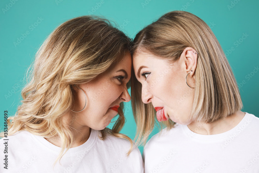 Portrait of cute twins blondes grimace each other isolated on green background Portrait of cute twins blondes grimace each other isolated on green background