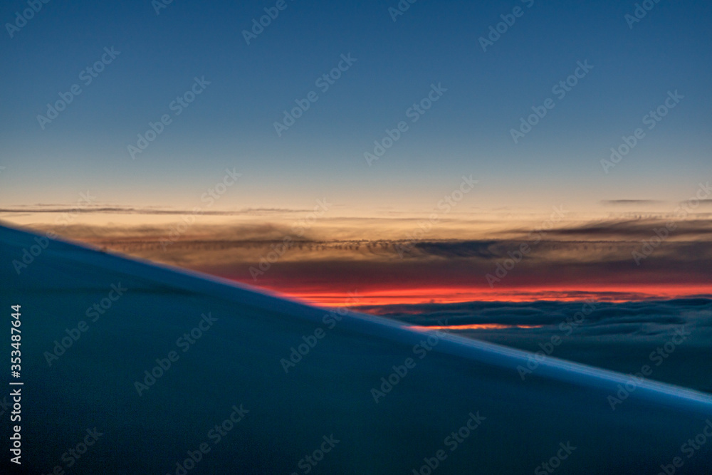 Aircraft wing silhouette seen through window in sunset sky with colorful clouds