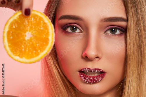 Girl closeup with orange with sugar on lips and on orange, isolated. Cosmetics, beauty concept