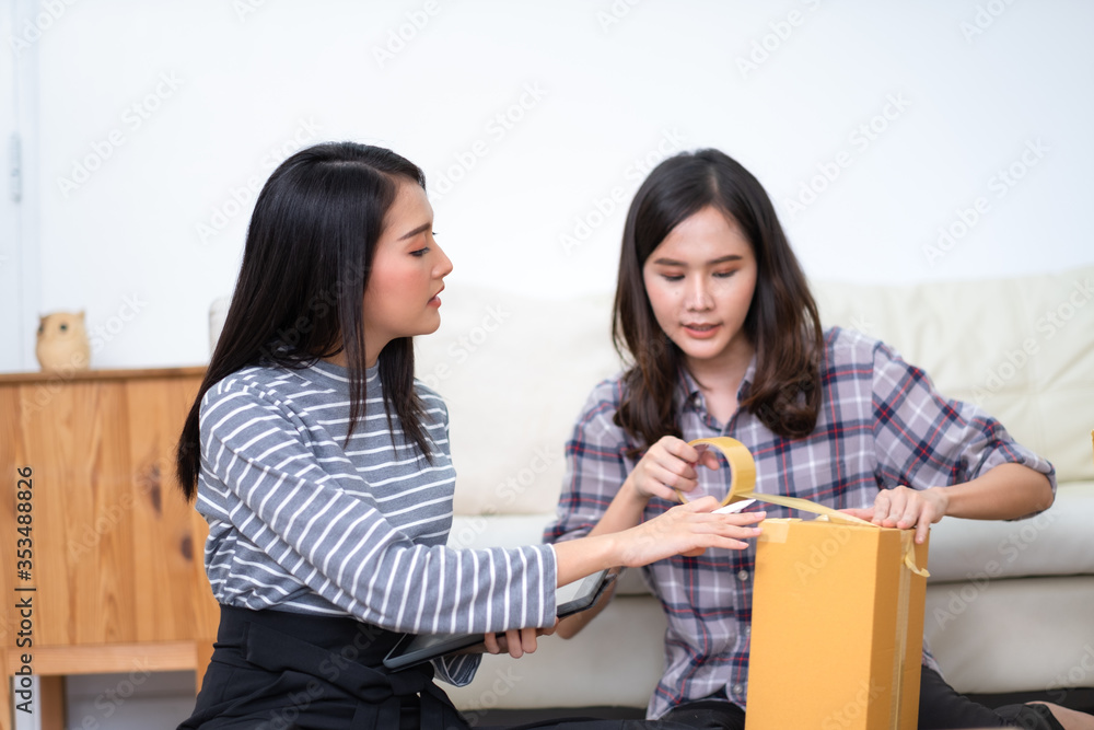 Two Asian female packing product and using tablet to checking order from customer shopping online and e-commerce at small office. Two Asian female packing product and using tablet to checking order from customer shopping online and e-commerce at small office.