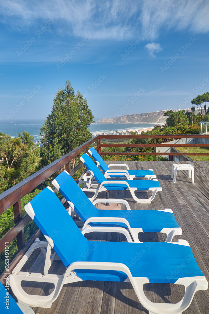 Blue sun loungers on a wooden terrace overlooking the sea.