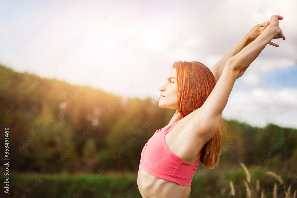A happy young woman in sportswear doing fitness in nature at sunset. Side view. Healthy lifestyle and outdoors fitness concept. Fitness and activity. Copy space. A happy young woman in sportswear doing fitness in nature at sunset. Side view. Healthy lifestyle and outdoors fitness concept. Fitness and activity. Copy space.