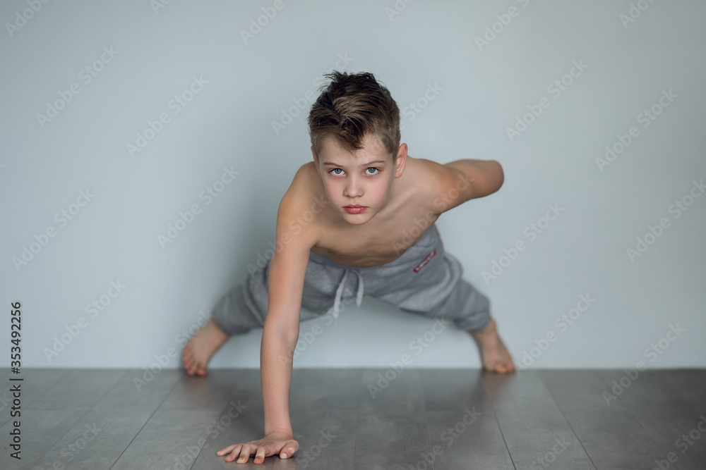The boy does push-ups from the floor on one arm at home. Quarantine and sport concept. The child develops perseverance and work on himself since childhood. The boy does push-ups from the floor on one arm at home. Quarantine and sport concept. The child develops perseverance and work on himself since childhood.