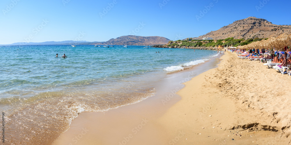 Pefkos beach with holiday-makers, sun beds and umbrellas in village of Pefkos - PANORAMA (Rhodes, Greece)