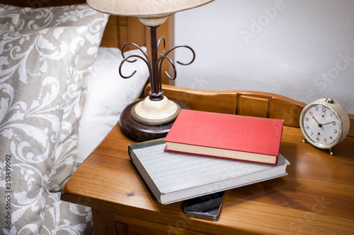 A red book and a grey book on the bedside table. Books on a mobile phone. Concept of digital disconnection. Reading time. Analog versus digital.