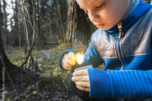 Little naughty boy sets fire to match in forest. Danger of child burns, attention. Careless handling of fire and flame, wildfire. Child holds burning torch in hands and plays. Dangerous firecrackers