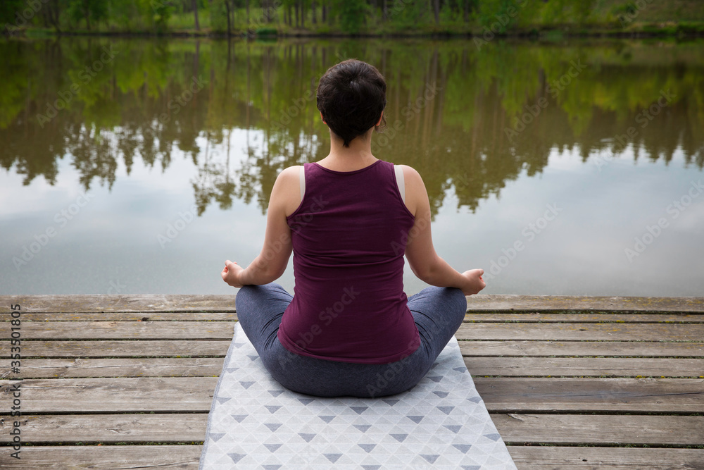 Fototapeta premium Young short-haired woman meditating by a lake. Wanderlust and mind peace concept.