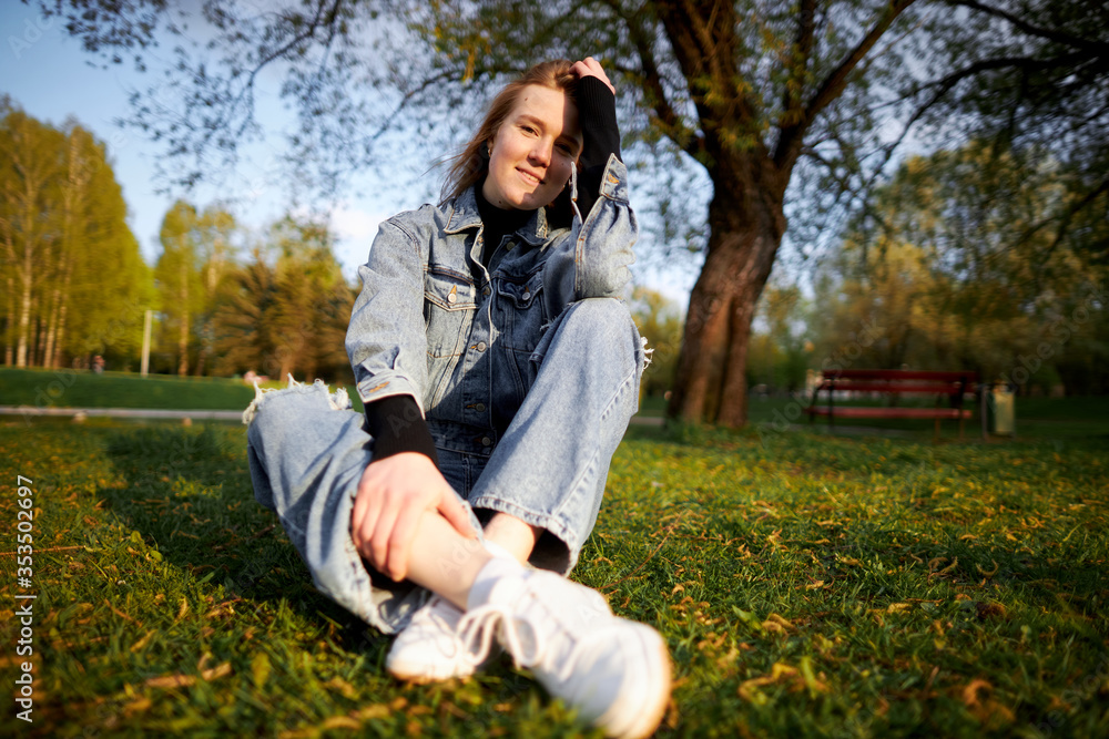red-haired teenage girl joyful sitting in jeans on green grass in the park on a sunny day red-haired teenage girl joyful sitting in jeans on green grass in the park on a sunny day