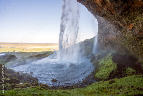 Seljalandsfoss during sunny day with lots of tourists infront and behind the waterfall.