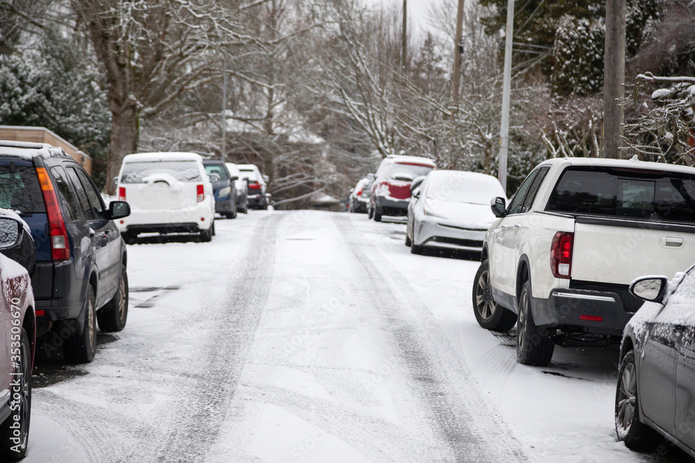 Snow covered residential street lined with parked cars