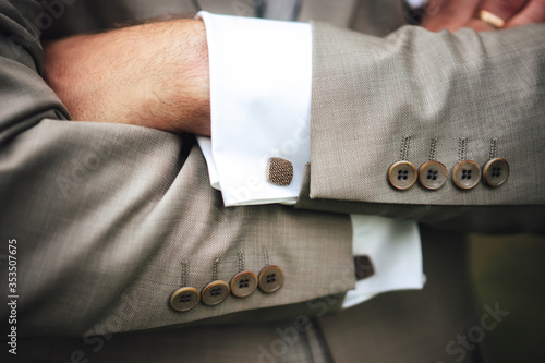Elegant businessman in gray suit with hands on chest. Close up image of male hands. Jacket sleeve buttons and cufflinks detail.