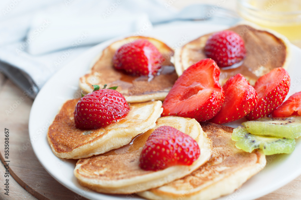 Breakfast with pancakes with strawberry, kiwi and honey on white background. Tasty breakfast for child on wooden board Breakfast with pancakes with strawberry, kiwi and honey on white background. Tasty breakfast for child on wooden board