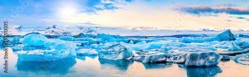 Icebergs float on Jokulsarlon glacier lagoon, with background mountain peaks lit by sunrise, in Iceland. photo