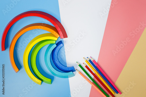 Wooden toy rainbow, arc and pencils on pink blue white orange background. Back to school background. Flat lay, top view. Educational games for kindergarten, preschool kids