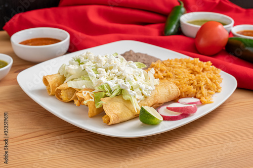 Chicken flautas topped with lettuce, cotija cheese and sour cream; served with refried beans and Spanish rice. A traditional Mexican dish served in the Americas. 
