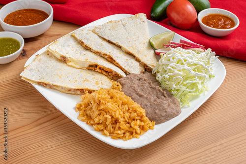 Cheesy chicken quesadilla made with a cheese blend, grilled chicken and a flour tortilla. Served in a Mexican restaurant with refried beans, Spanish rice, lettuce, and radish.