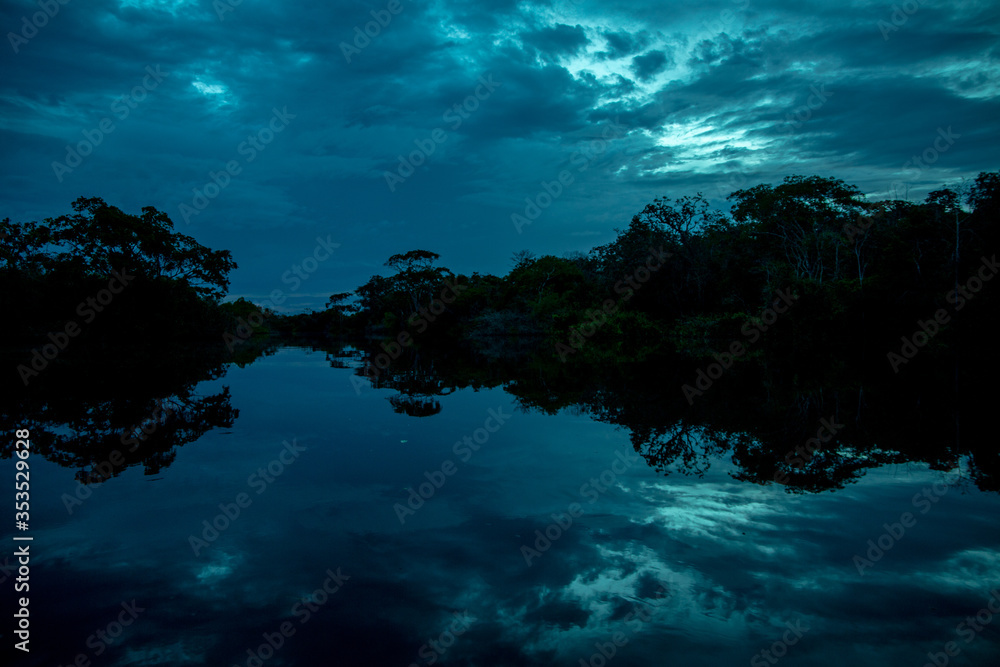 Blue Dark Dramatic River at Sunset with a Perfect Reflection of the Trees and Clouds on the Water