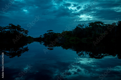 Blue Dark Dramatic River at Sunset with a Perfect Reflection of the Trees and Clouds on the Water © Paradox