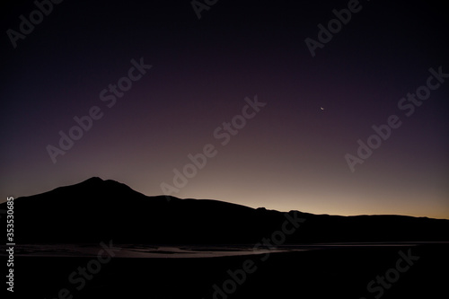 Clear Dark Purple Sky with the Moon and Stars at Night above a Mountain Range by a Lagoon