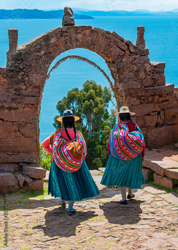 Two Peruvian Quechua indigenous women in traditional clothes walking through the arch of the rulers on Taquile island with the Titicaca Lake, Peru. photo