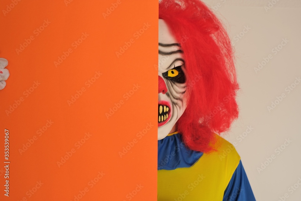 Fototapeta premium Halloween holiday concept. Evil clown with an orange sheet of paper in his hands.copy space.Portrait of a scary evil clown on white background. 