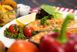Delicious fillet cut salmon steak in white plate side dish with french fries and salad on dark wood background