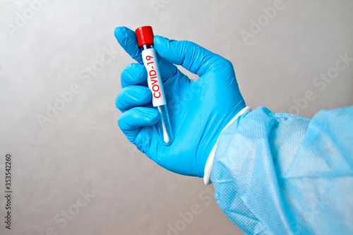 Hand in blue medical disposable rubber gloves holding a tube with a tuffer for analysis on a gray background with the inscription COVID-19 photo