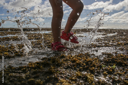 Child in rubber red sandals jumping up and down and splashing the water