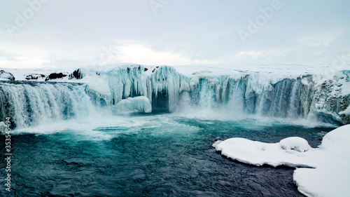 Low angle photo if a wide waterfall in northern Iceland. The waterfall is partly frozen but the cold water escapes its ice cover. The photo is taken from the surface of the water.