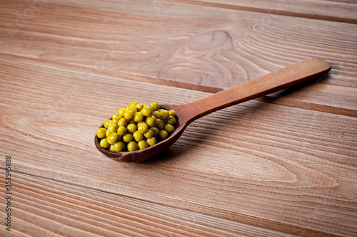 Canned green peas in a wooden spoon lying on a wooden surface of the table.