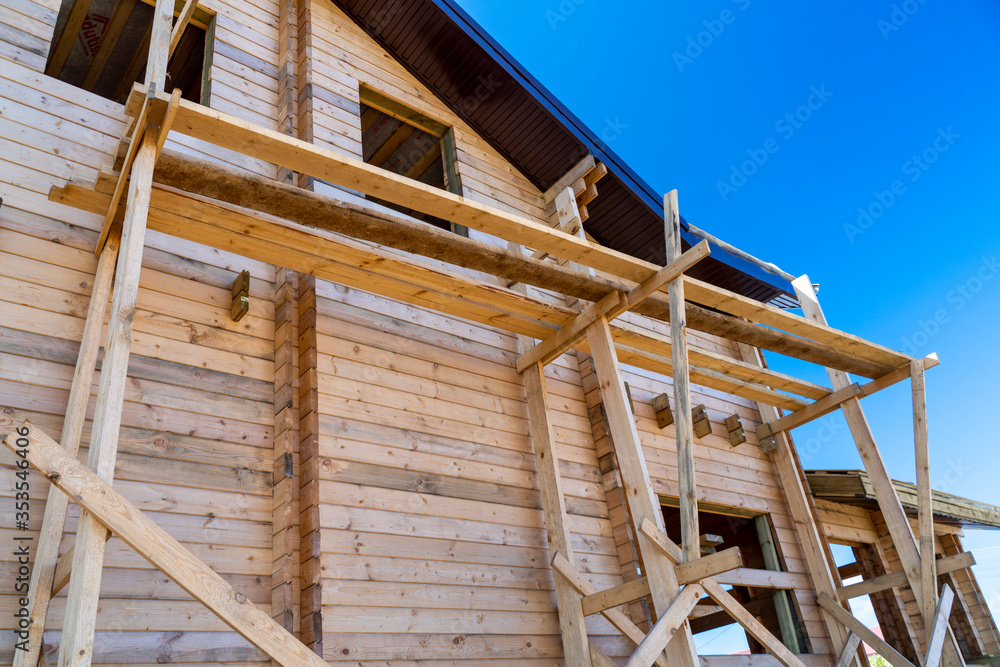 The house with a wooden structure is being built surrounded by scaffolding, blue sky. The house with a wooden structure is being built surrounded by scaffolding, blue sky.