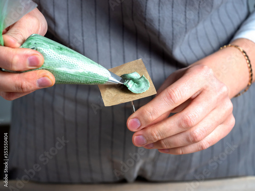 professional pastry chef makes flowers from cream. Confectioner hands squeeze cream from a pastry bag.  green cream in a pastry bag. cream petal for cake decorating.  on wooden background. 