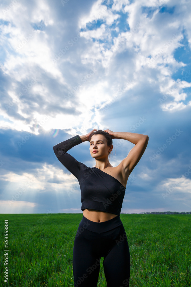Young woman of athletic build with a black top and black leggings on a background of blue sky. Healthy lifestyle, athletic brunette girl. The concept and motivation of sports Young woman of athletic build with a black top and black leggings on a background of blue sky. Healthy lifestyle, athletic brunette girl. The concept and motivation of sports