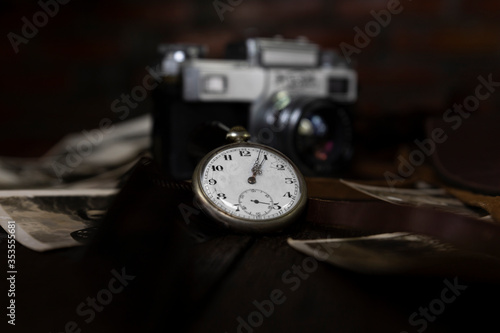 Vintage pocket watch, film camera and old photographs on a rustic surface