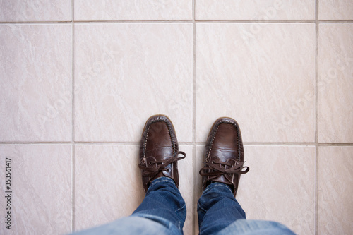 Legs in Jeans and brown leather shoes against tiled floor. Concept of waiting with space for text.