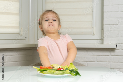Bilde på lerret a little girl sits at a table in the kitchen and pushes away a plate of vegetables